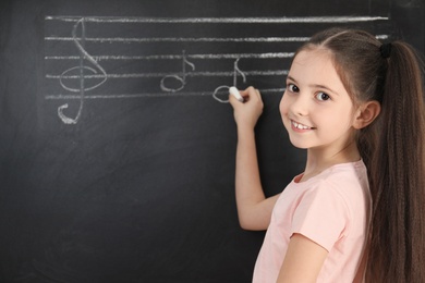 Little girl writing music notes on blackboard. Space for text