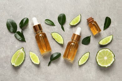 Glass bottles of bergamot essential oil and fresh fruits on light grey table, flat lay
