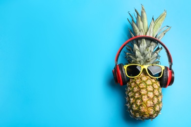 Top view of pineapple with headphones and sunglasses on light blue background, space for text. Creative concept