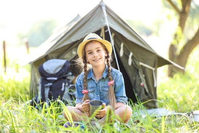 Little girl with mug near tent outdoors. Summer camp