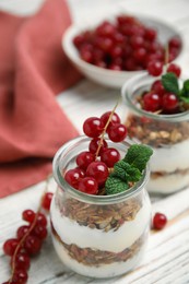 Delicious yogurt parfait with fresh red currants and mint on white wooden table, closeup