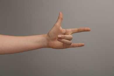 Woman showing gesture of horns on grey background, closeup