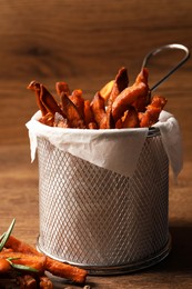 Frying basket with sweet potato fries on wooden table, closeup