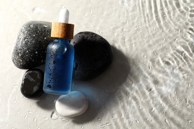 Bottle of face serum and spa stones in water on light background, space for text