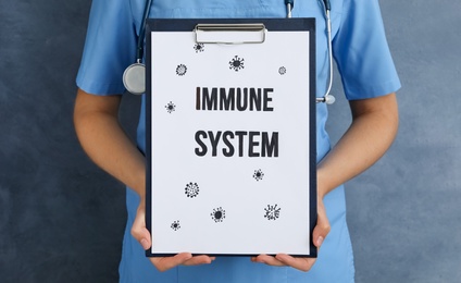 Woman holding clipboard with phrase Immune System on blue background, closeup