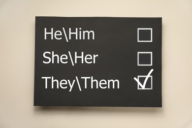 Gender equality. Small blackboard with written pronouns on beige background, top view