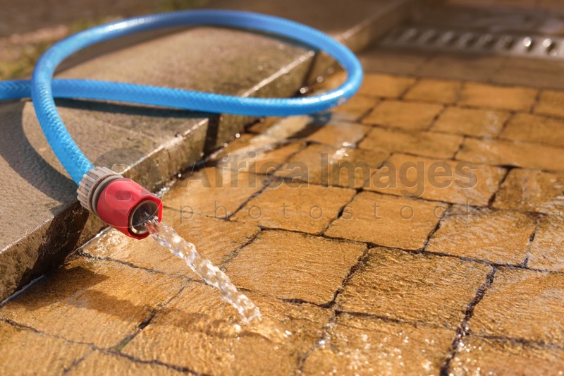Photo of Water flowing from hose on stone floor outdoors, closeup. Space for text