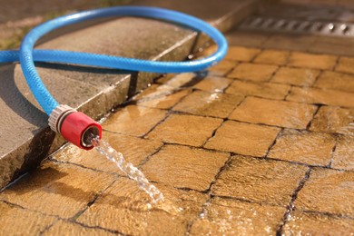 Photo of Water flowing from hose on stone floor outdoors, closeup. Space for text