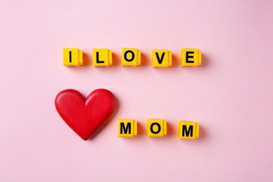 Phrase I LOVE MOM made of plastic letters and wooden heart on color background, top view