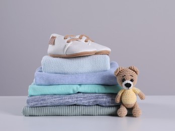 Stack of clean baby's clothes, toy and small shoes on table against light grey background. Space for text