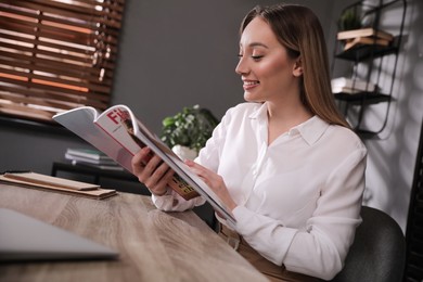 Happy woman reading magazine at workplace in office