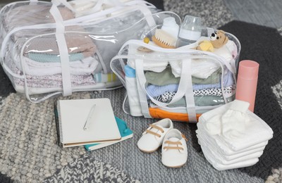 Packed bags for maternity hospital, notebooks and baby stuff on carpet