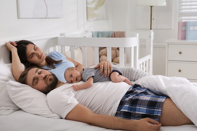 Tired young parents with their baby sleeping in bed at home