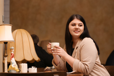 Beautiful overweight woman at table in cafe. Plus size model
