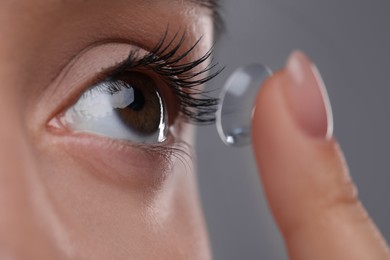 Closeup view of young woman putting in contact lens on grey background
