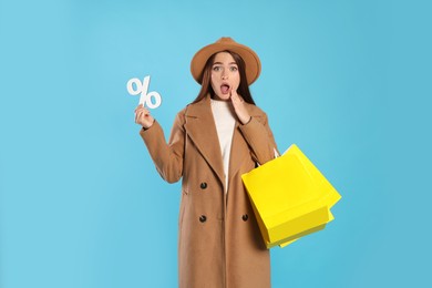 Photo of Surprised young woman with shopping bags and percent symbol on light blue background. Big sale