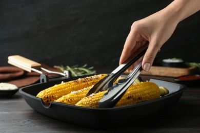 Photo of Woman taking corn with tongs from grill pan, closeup