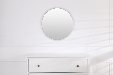 Photo of Trendy round mirror and chest of drawers near white wall. Interior element