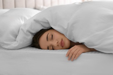 Young woman covered with warm white blanket sleeping in bed at home