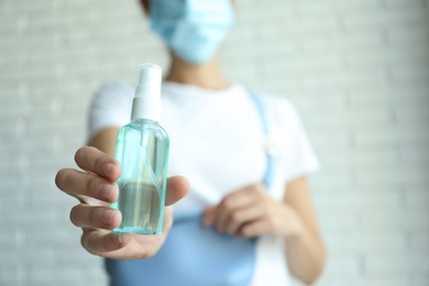Woman holding hand sanitizer against blurred background, closeup. Personal hygiene during COVID-19 pandemic
