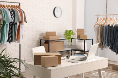 Store interior with clothing racks, cardboard boxes and laptop. Online selling