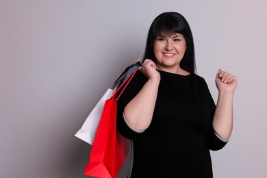 Beautiful overweight mature woman with shopping bags on light grey background. Space for text