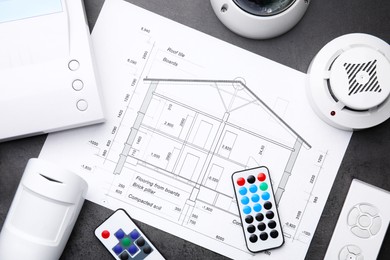 Building plan, remote controls, smoke and movement detectors on grey table, flat lay. Home security system