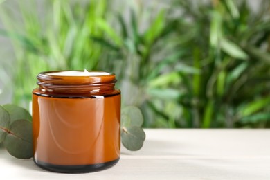 Jar of hand cream and eucalyptus branch on white table, space for text