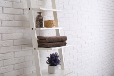 Clean soft towels and plant on shelves near white brick wall. Space for text