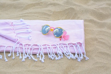 Photo of Blanket with stylish sunglasses and flower on sand outdoors. Beach accessories