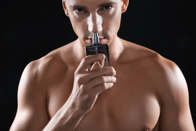 Handsome young man smelling bottle of perfume on black background
