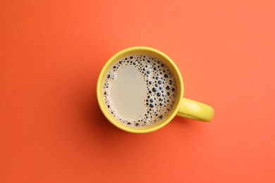 Yellow mug of freshly brewed hot coffee on orange background, top view