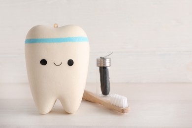 Tooth model with cute face, toothbrush and dental floss on white wooden table. Space for text