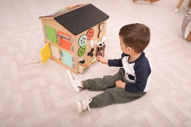 Little boy playing with busy board house on floor in room