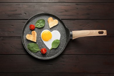 Romantic breakfast with heart shaped fried egg, toasts, spinach and tomatoes in pan on wooden table, top view