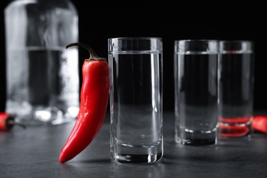 Red hot chili peppers and vodka on grey table against black background