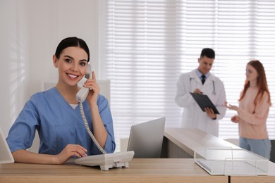 Receptionist talking on phone while doctor working with patient in hospital