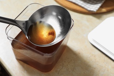 Photo of Container and ladle with used cooking oil on beige table