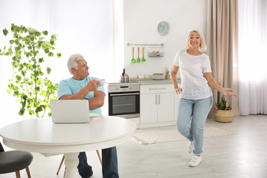 Middle aged woman dancing near her husband in kitchen. Happy mature couple