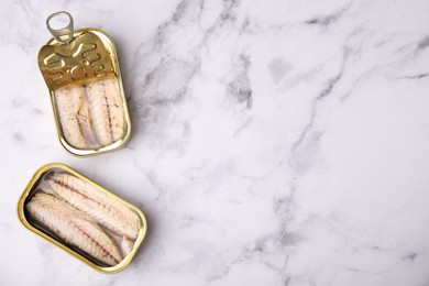 Photo of Open tin cans with mackerel fillets on white marble table, flat lay. Space for text