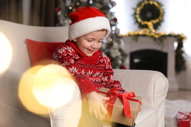 Cute little boy holding gift box in room decorated for Christmas