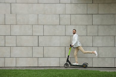 Businessman riding modern kick scooter near grey stone wall outdoors, space for text