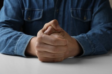 Photo of Man clenching hands at table while restraining anger, closeup
