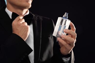 Young man with perfume bottle on black background, closeup