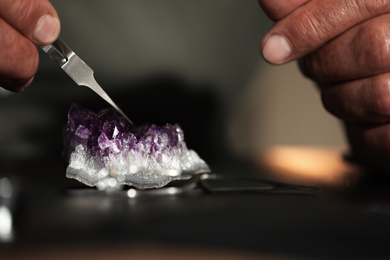 Professional jeweler working with beautiful amethyst at table, closeup