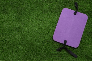 Violet foam tourist seat mat on green grass, top view. Space for text