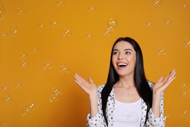 Young woman having fun with soap bubbles on yellow background, space for text