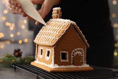 Woman decorating gingerbread house with icing at table, closeup