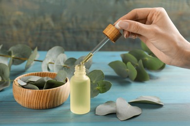 Woman taking eucalyptus essential oil with dropper from bottle at light blue wooden table, closeup