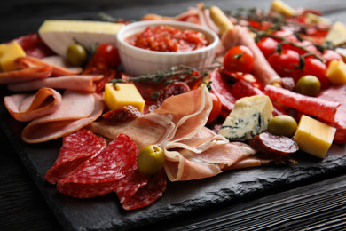 Photo of Tasty ham with other delicacies served on black wooden table, closeup